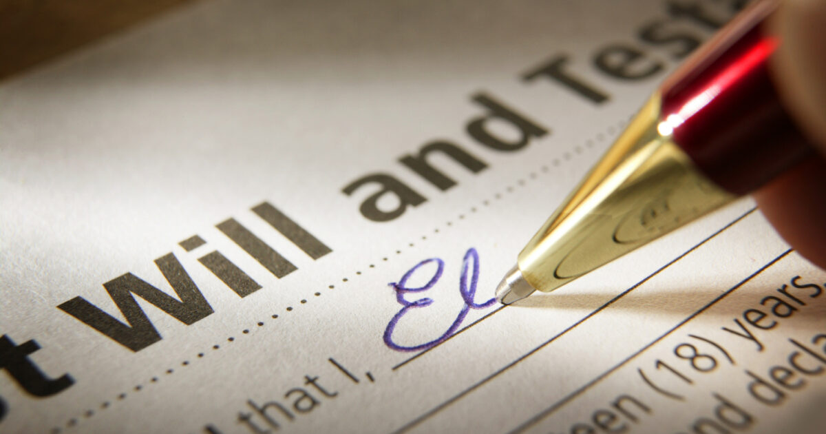 Signing Last Will and Testament. A shallow depth of field focuses putting the pen to paper finalizing the process of securing one's legacy. A red and gold ballpoint pen writes in blue ink and the writer begins to commit their name to paper in elegant blue cursive.  A pleasant reflection bounces off the gold pen.