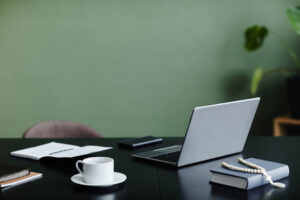 Office workplace desk with open laptop against green wall