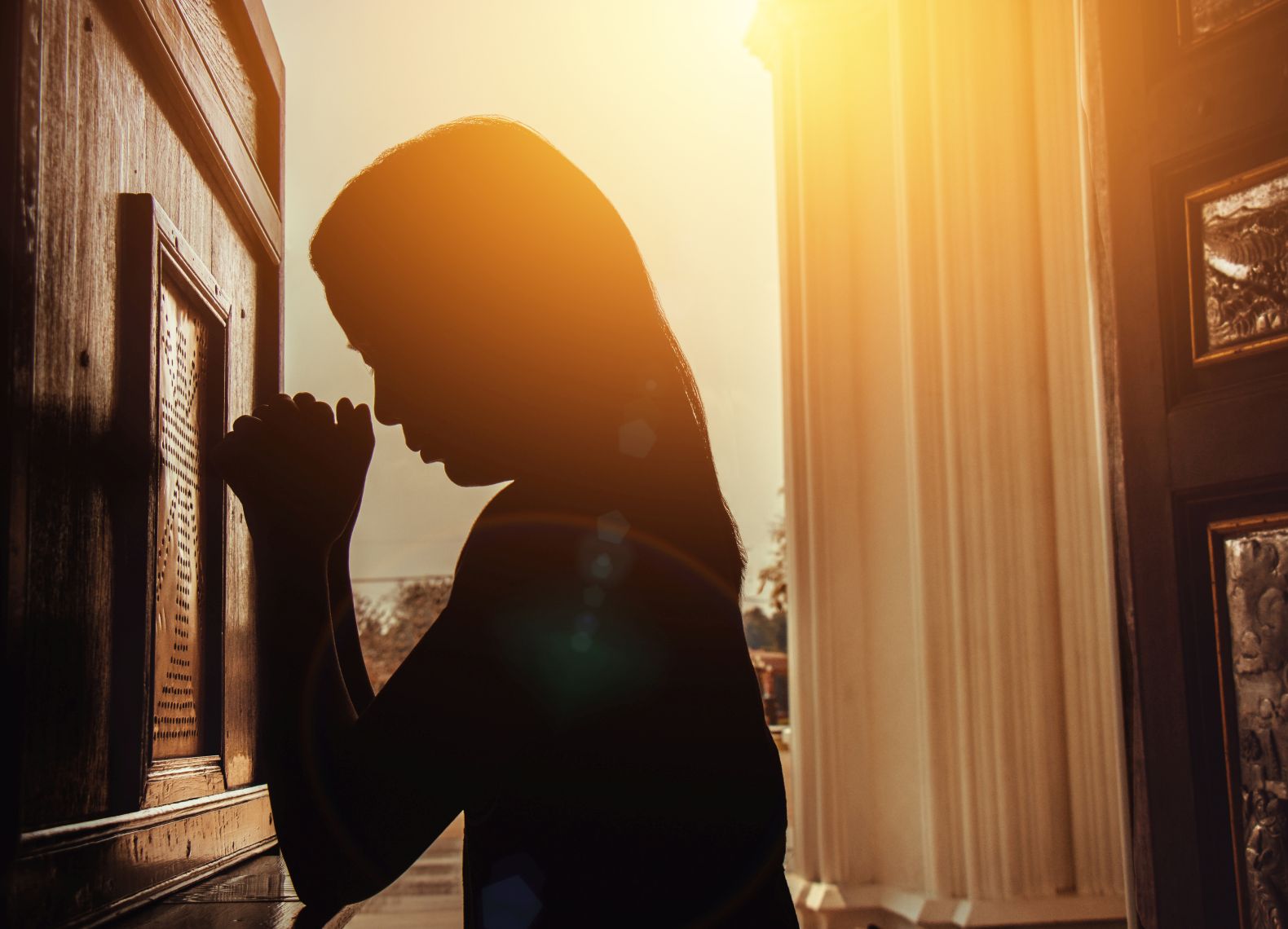 silhouette of woman kneeling and praying in modern church at sunset time