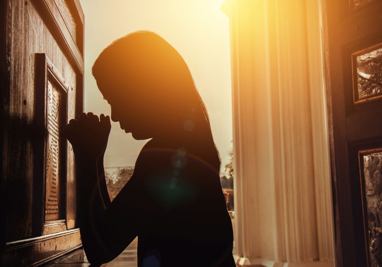 silhouette of woman kneeling and praying in modern church at sunset time