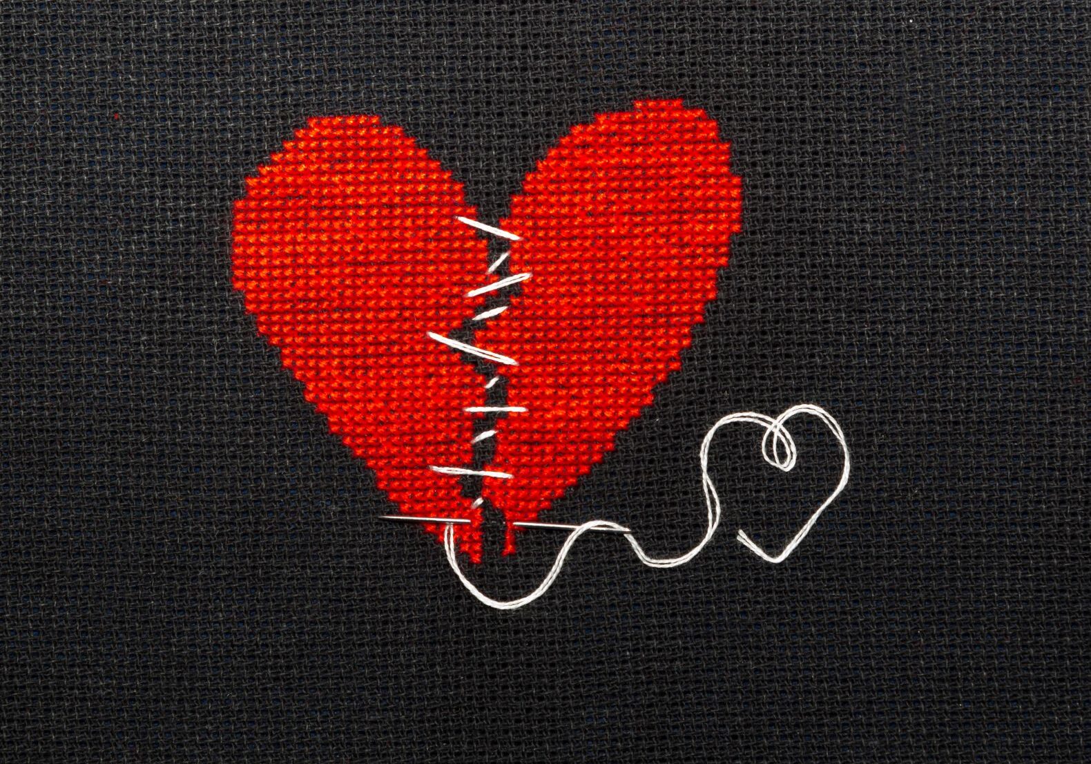 Two halves heart embroidered red thread on black fabric. Two halves heart sewn with black thread.