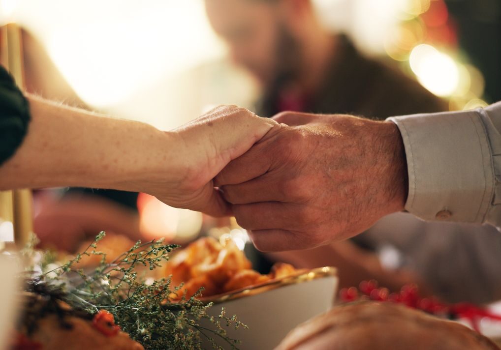 Holding hands, Christmas and prayer with family at dinner table for gratitude, holiday season and love. Worship, spiritual and support with closeup of people in home for festive celebration and trust